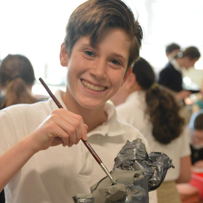 YC student holding paintbrush and painting ceramics