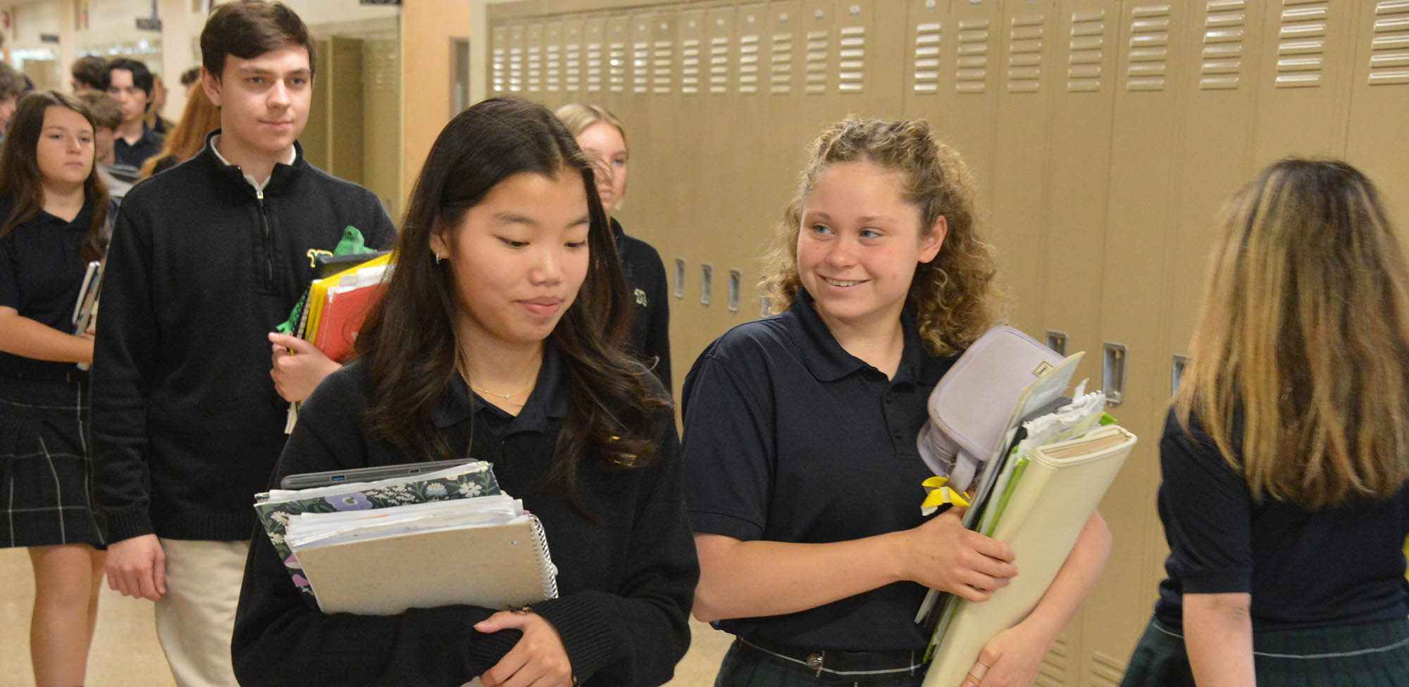 teenage YC students walking through hallway with books in their hands
